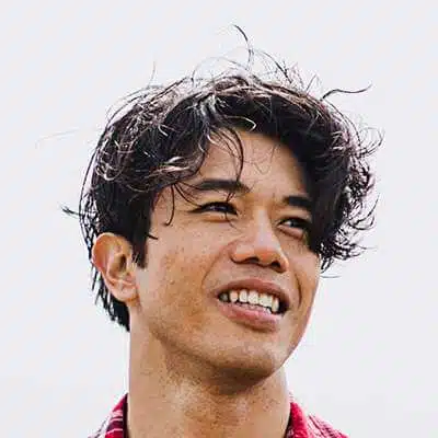 Mr. H in a jewelry showroom, inspecting a luxury wristwatch while wearing a navy blazer, black turtleneck, gold chain, and silver watch.